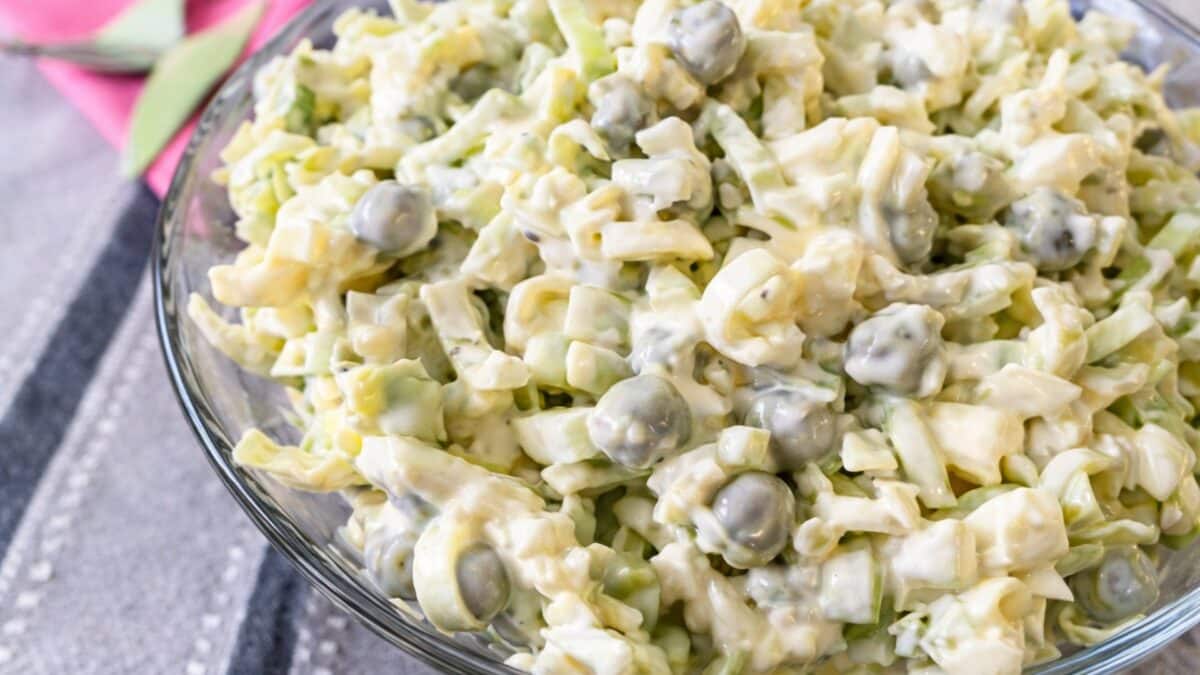 Tradycyjna sałatka z pora i zielonego groszku z jajkiem podana w szklanej misce, ukazująca chrupiącą strukturę pora i kremowy sos majonezowy.