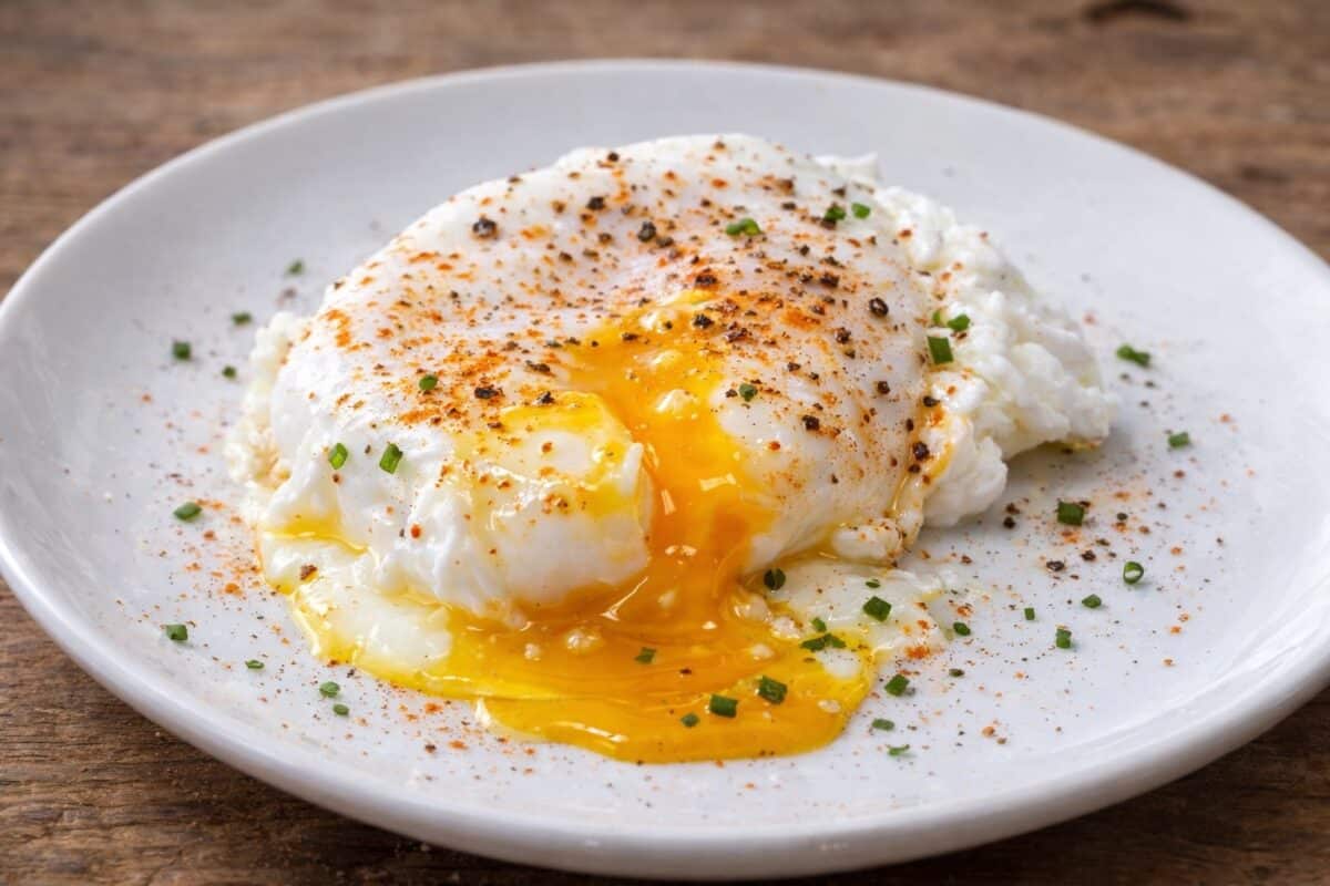 Jajko po wiedeńsku podane w szklance z masłem i szczypiorkiem na drewnianym stole.