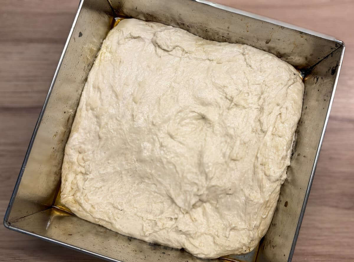Luźne ciasto na focaccię rozciągnięte na blasze posmarowanej oliwą