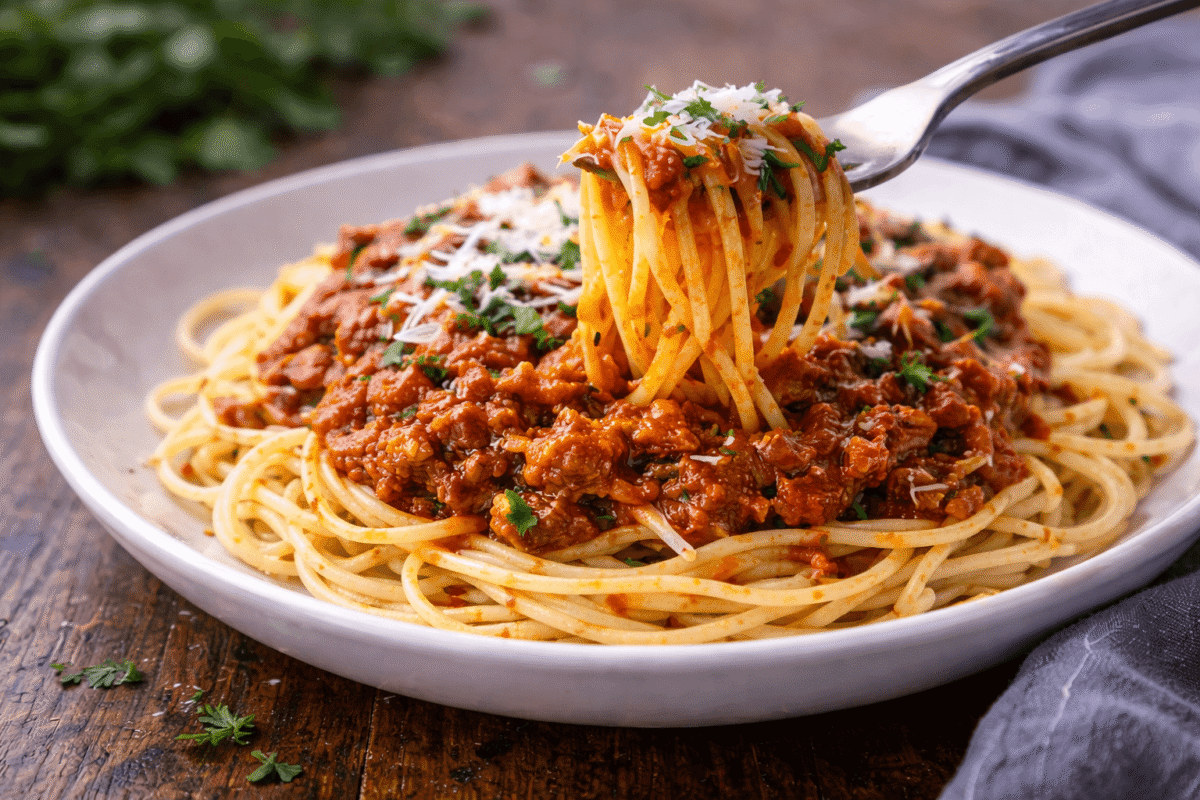 Zbliżenie na apetyczny makaron spaghetti z gęstym sosem pomidorowo-mięsnym i drobinkami sera na talerzu.