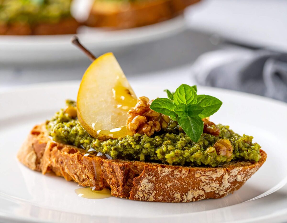 Chrupiące grzanki z pesto z nerkowców, plasterkami gruszki i strużką miodu na ceramicznym talerzu.