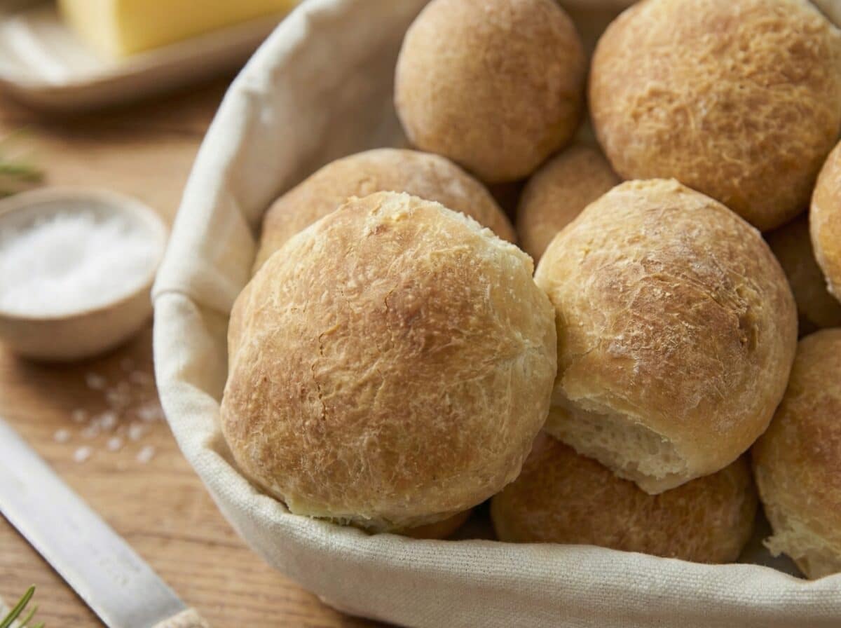 Zbliżenie na koszyk z domowym pieczywem, ukazujące chrupiącą, delikatnie popękaną skórkę i fakturę świeżych bułek.