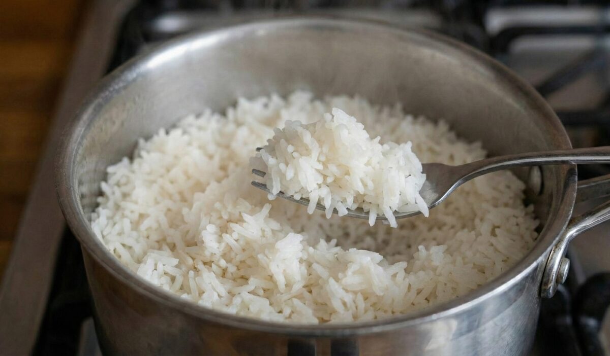 Zbliżenie na wnętrze garnka ze świeżo ugotowanym białym ryżem. Widelec delikatnie unosi porcję ziaren, pokazując, że są one puszyste, oddzielone od siebie i niesklejone w papkę. Z ryżu unosi się delikatna para.