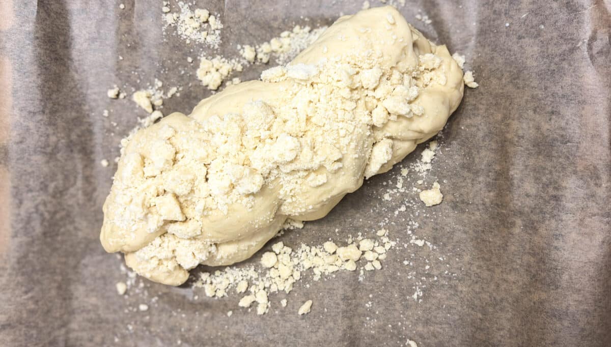 Zapleciona surowa chałka drożdżowa posypana kruszonką przed włożeniem do piekarnika.