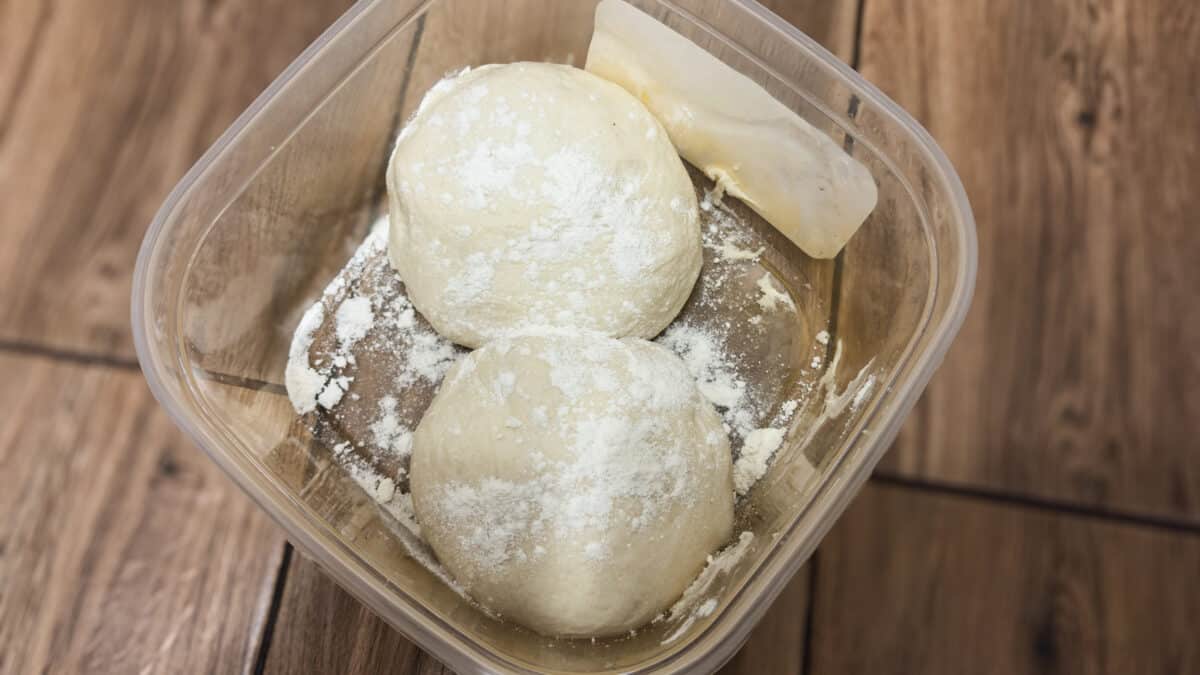 Pizza rzymska z szynką parmeńską i rukolą 2 Dwie kulki ciasta na pizzę rzymską oprószone mąką i wyrastające w pojemniku.