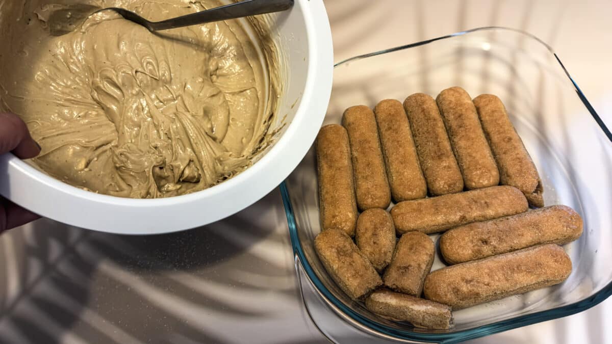 Tiramisu pistacjowe – kremowy włoski deser bez pieczenia 3 Warstwa biszkoptów nasączonych espresso obok miski z kremem do tiramisu pistacjowego