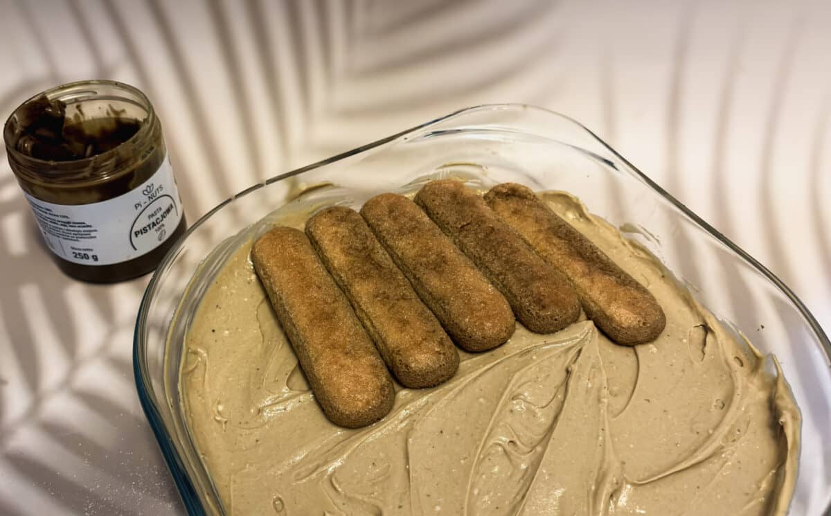 Tiramisu pistacjowe – kremowy włoski deser bez pieczenia 4 Układanie drugiej warstwy biszkoptów na kremie pistacjowym z pastą Pi-Nuts
